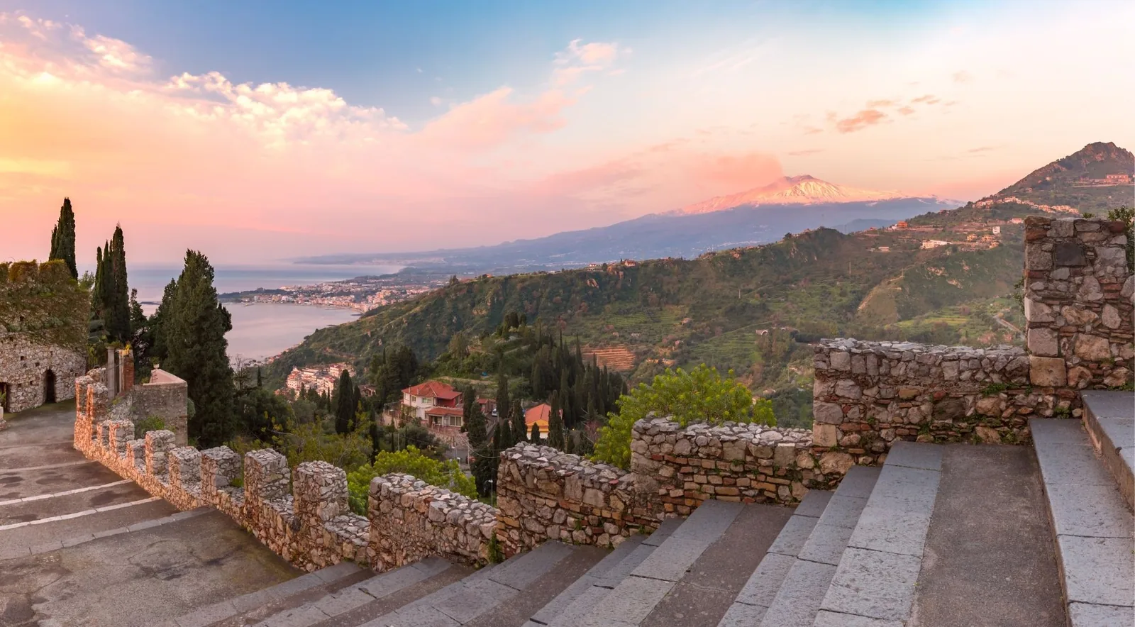 The stone terrace of Taormina looking across the bay to a snow-capped Mount Etna at sunrise
