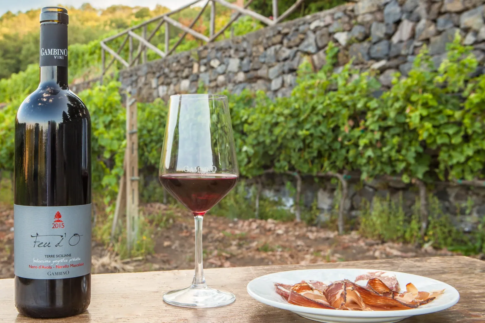 A bottle and a poured glass of Etna red against a dry lava-stone wall