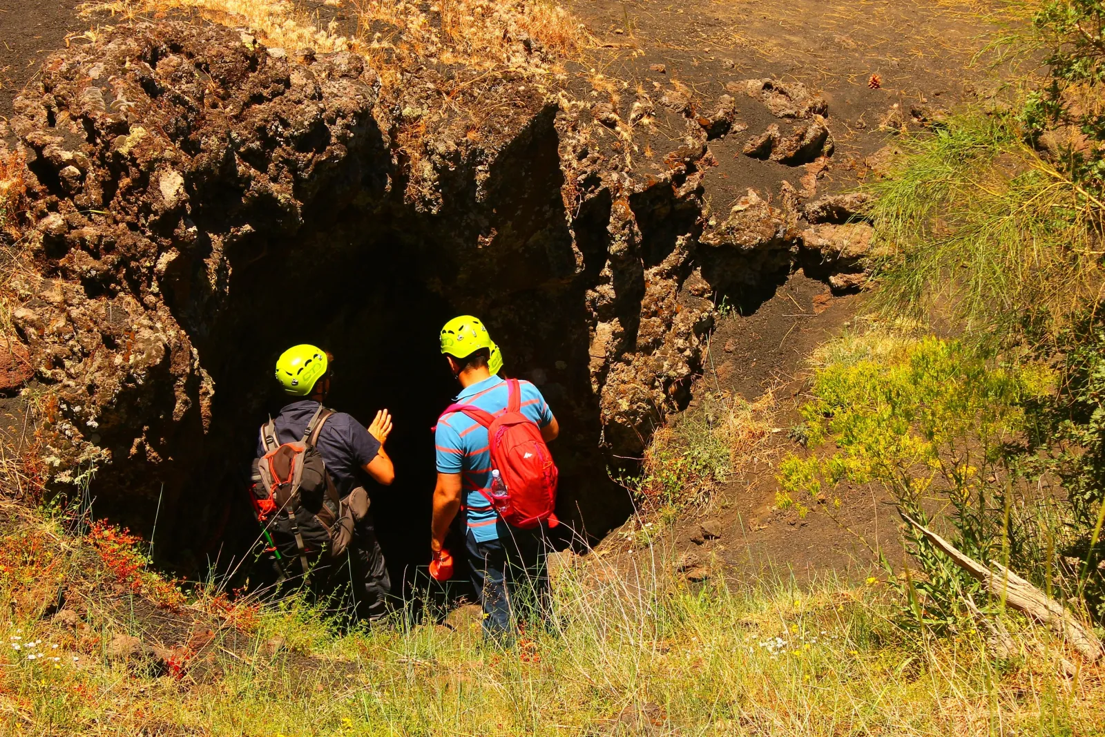 Two visitors in helmets and headlamps at the mouth of a lava cave