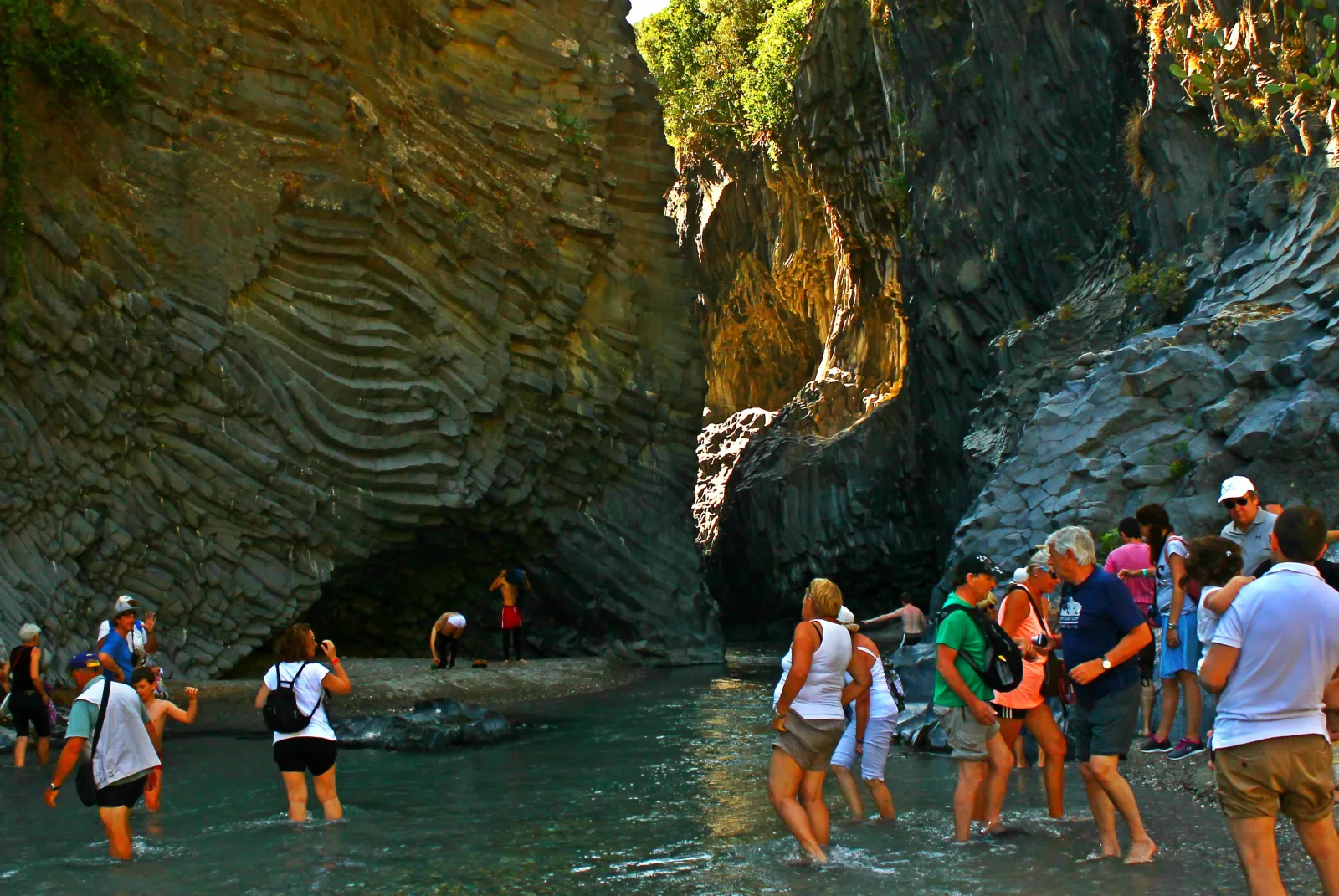 Visitors wading the shallow Alcantara river between its dark basalt walls
