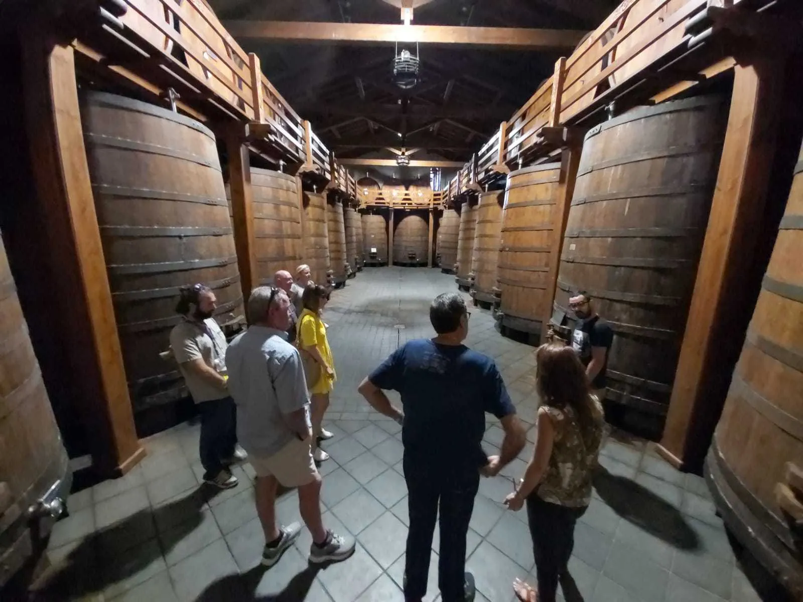 Visitors walking a long corridor of stacked barrels inside the first winery