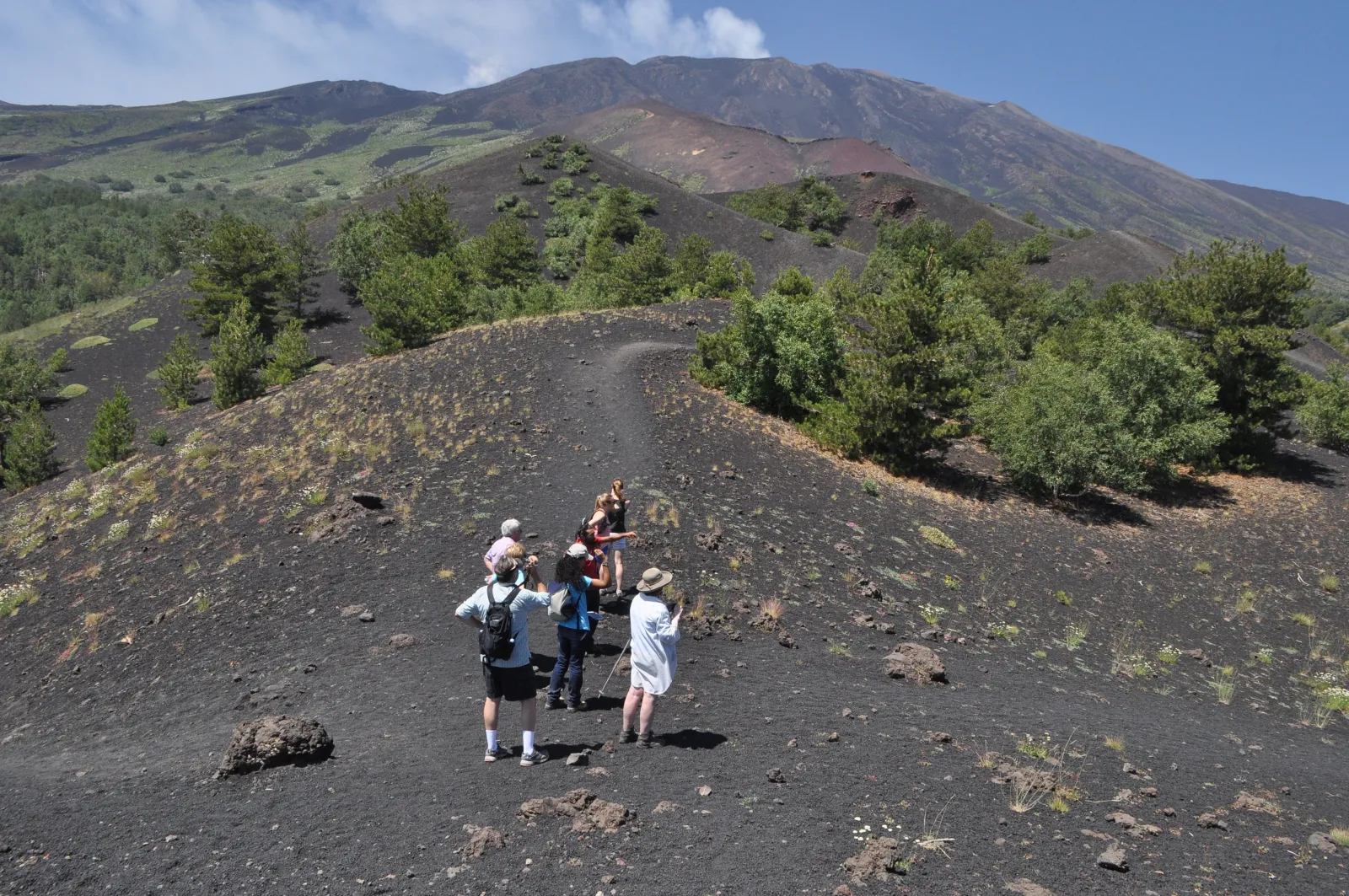 Walkers on a black cinder slope below the rim of an extinct crater